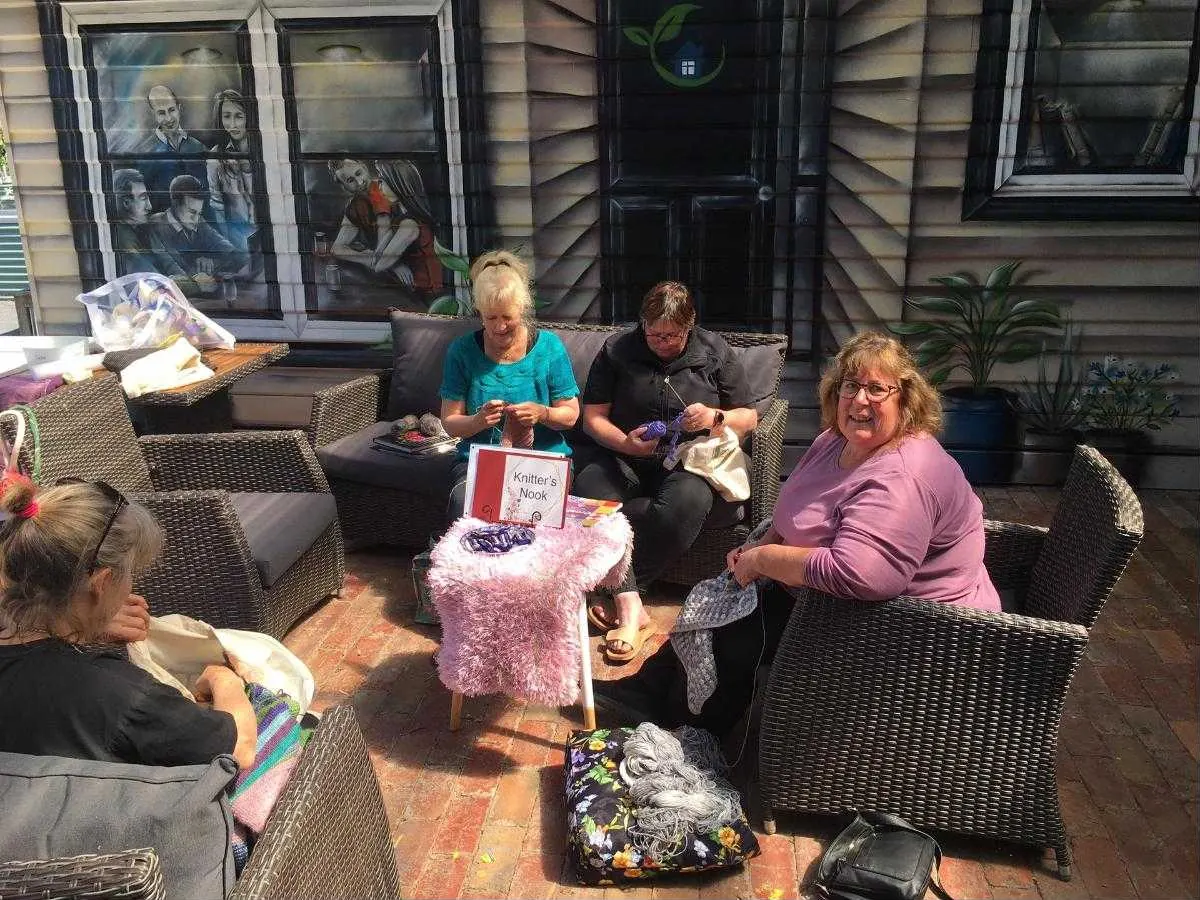 The Knitters Nook group knitting on the Centre's back verandah in front of the painted mural