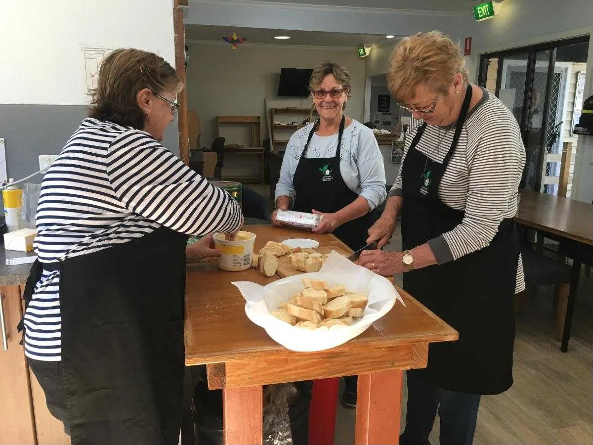Two volunteers in Centre aprons preparing bread for a community lunch