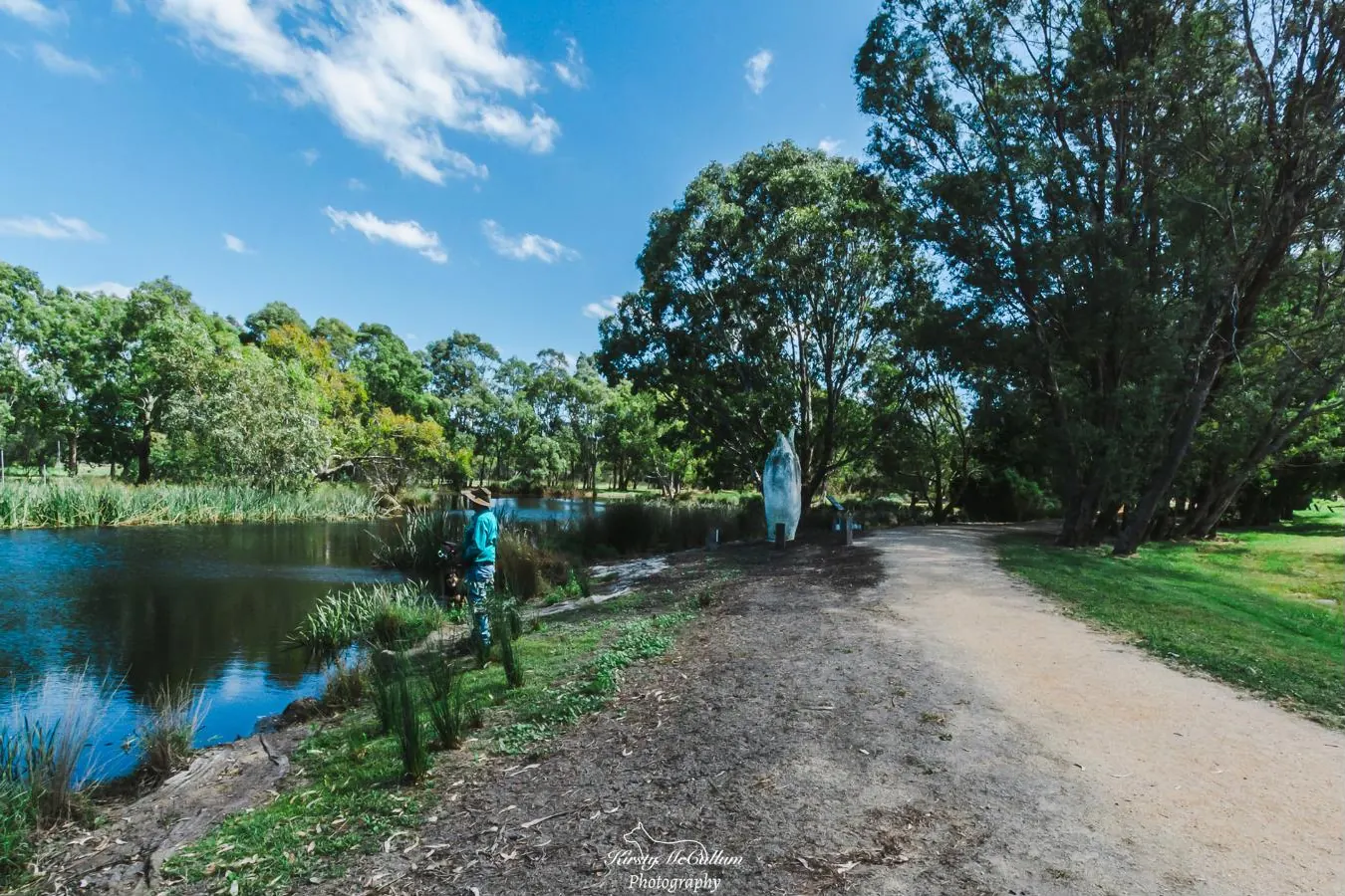 A man fishing beside the water at the Heyfield Wetlands under a blue sky